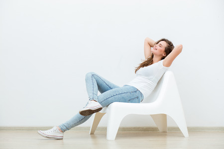single happy young woman sitting on a white chair in an empty room, thinking on somethingの写真素材