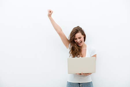 young beautiful modern woman having an laptop in hands, leaning on a white wall, happyの写真素材