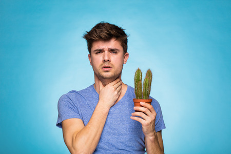 concept with a young man in T-shirt, holding in hand a cactus suggesting painの写真素材