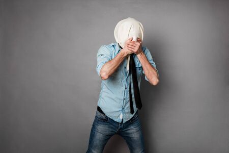 concept with a young man with face covered by a textile material acting normal but having no face, on greyの写真素材
