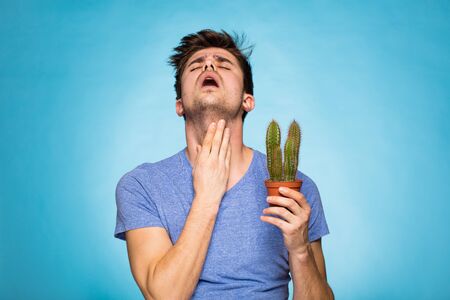 concept with a young man in T-shirt, holding in hand a cactus suggesting painの写真素材