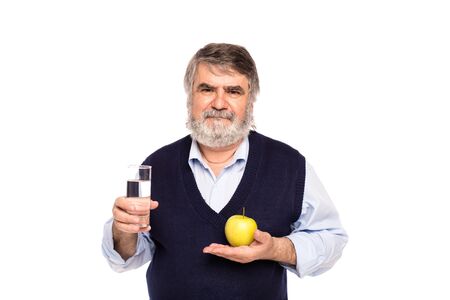 old man with gray beard having a glass of water and green apple in hands, isolated on whiteの写真素材