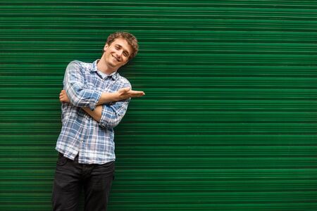 Smiling young man casual dressed standing against green background,  showing one sideの写真素材