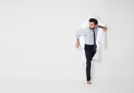 young office man with tie and barefoot breaking the paper background, passing from side to side, looking very curious to one sideの写真素材