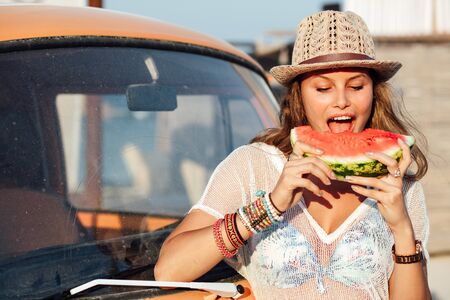 young pretty women with slice of watermelon standing on a old hippie van, in sunlight