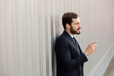 businessman with beard and elegant suit having an idea while standing outside against a gray wallの写真素材