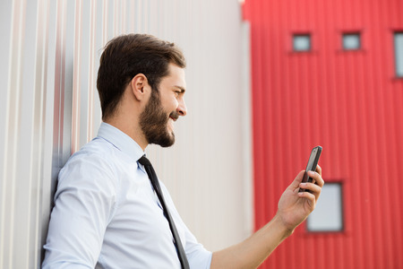 office man smiling at his cellphone outside in a work breakの写真素材