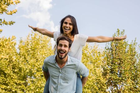 holidays, vacation, love and friendship concept - smiling couple having fun, woman with open hands...