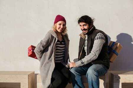 nice joyful couple standing outside on a bench and exchanging giftsの写真素材
