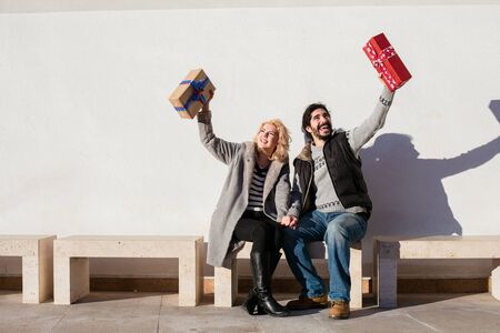nice joyful couple standing outside on a bench and exchanging giftsの写真素材