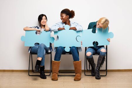 group of three different ethnic woman waiting in chairs with puzzle piecesの写真素材