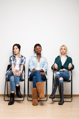concept of diversity with three different women, asian, caucasian and afro american sitting on chair wainting for interviewの写真素材
