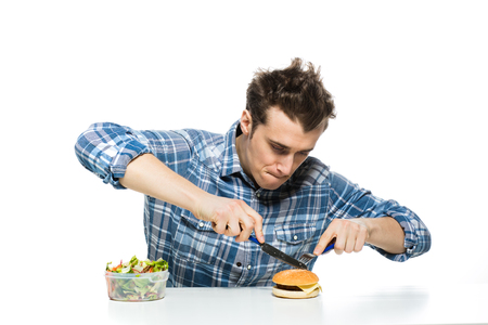 fast food versus healthy food concept with young man eating a hamburger and leaving salad apartの写真素材