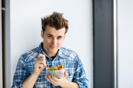 young man eating his vegan salad from a plastic box, his take away lunch at workの写真素材