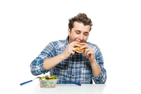 fast food versus healthy food concept with young man eating a hamburger and leaving salad apartの写真素材