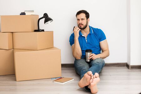 young man lying on the floor with packing boxes near and coffee can for energyの写真素材