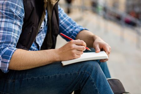 nice student sitting on university stairs outside writing something on his notebookの写真素材