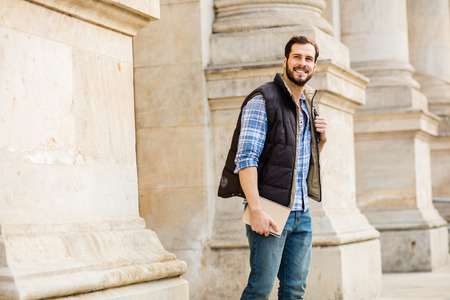 smiling student with books and backpack in front of university leaving classesの写真素材
