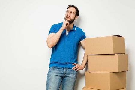 adult man standing next to a stack of carton boxes on white wallの写真素材