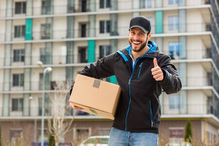 Delivery man with cap and cardboard in hands, with blocks behindの写真素材