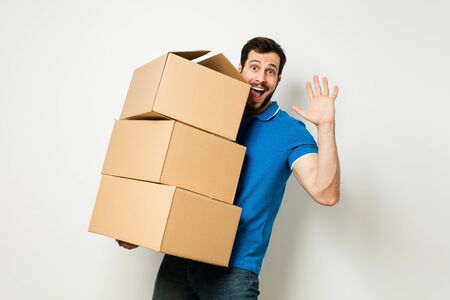 bearded young man in blue shirt carrying three carton boxes on a white wallの写真素材