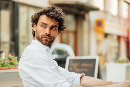 handsome masculine man sitting at terrace alone, elegant dressed, outdoorの写真素材