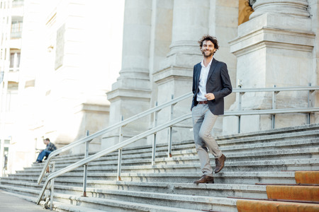 elegant and modern man walking down stairs of important building with positive attitudeの写真素材