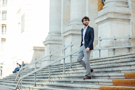 elegant and modern man walking down stairs of important building with positive attitudeの写真素材