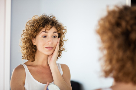 young curly woman using skin cream on in a mirrorの写真素材