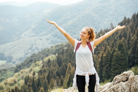 portrait of a young and beautiful woman with her backpack in the mountains looking at camera very happyの写真素材