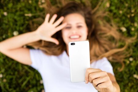 beautiful young woman talking at mobile phone lying in green grass