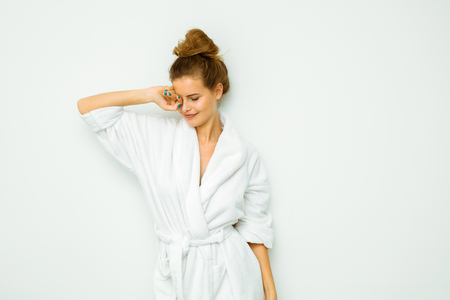 young beautiful woman standing on a white wall in bath towel sleepyの写真素材