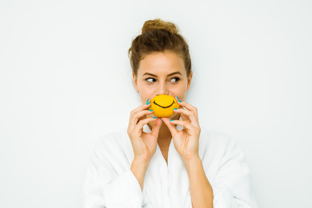 young beautiful woman standing on a white wall in bath towel playing with her favorite fruit, the lemonの写真素材