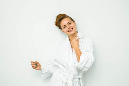 young beautiful woman standing on a white wall in bath towel standing and looking to cameraの写真素材