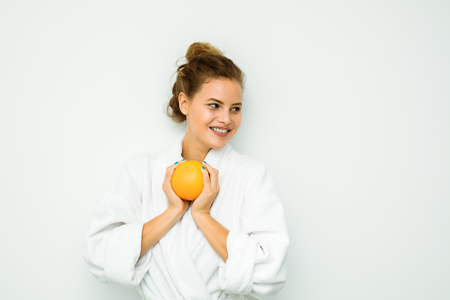 young and beautiful woman in a bathrobe on white wall smiling and having a grapefruit in handsの写真素材