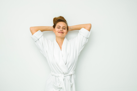 young beautiful woman standing on a white wall in bath towel standing and looking to cameraの写真素材