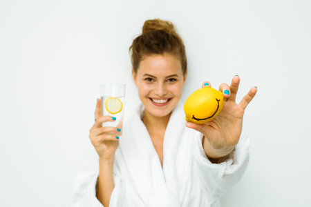 young beautiful woman standing on a white wall in bath towel playing with her favorite fruit, the lemonの写真素材