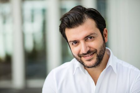 succesfull man in white shirt standing next to an office bulilding in a small break outside in a corporate areaの写真素材