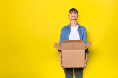 pretty woman standing on yellow background with moving cardboard box