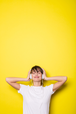 young and beautiful woman listening music with white headphones on isolated on yellow backgroundの写真素材