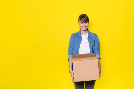 pretty woman standing on yellow background with moving cardboard boxの写真素材