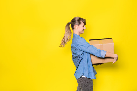pretty woman standing on yellow background with moving cardboard boxの写真素材