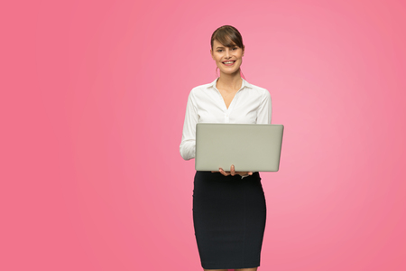 beautiful young businesswoman checking the statistics on laptop, isolated on pink backgroundの写真素材