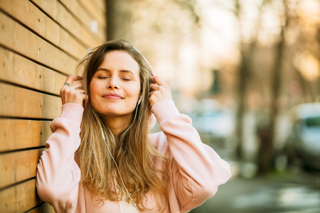 cool hipster young girl in pink hoodie standing against a wooden wall on the streetの写真素材