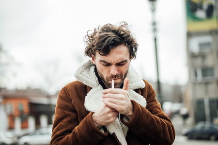 cool handsome man smoking cigarette outside in a aviator coat with masculine attitude waiting for someの写真素材
