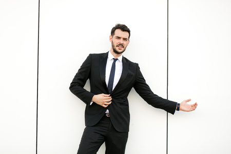 elegant man in suit, businessman, presenter, standing on white wall interacting with free space aroiund him, presenting his side with joyの写真素材