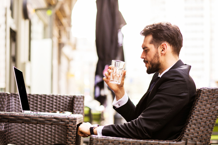 Portrait of handsome successful man drink coffee and look to the digital tablet screen sitting in coffee shop, business man drinking water in a break and trying to relaxの写真素材