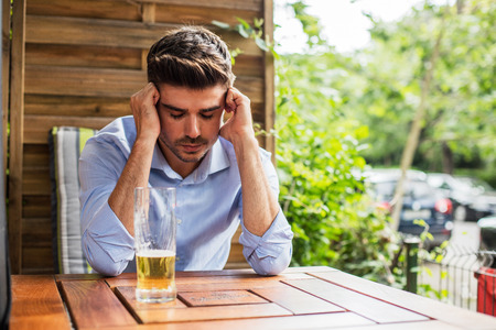 alcohol addiction. handsome young man with glass of beer in front thinking or regretting something