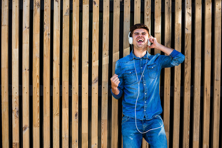 handsome sexy man in jeans outfit, on wooden background, with free space for text next to him, listening music and dancing and screamingの写真素材
