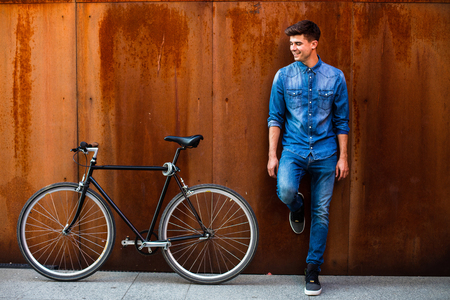concept of a cool transportation in a city with a fashionable guy in jeans outfit next to his single speed bike on a rusty backgroundの写真素材